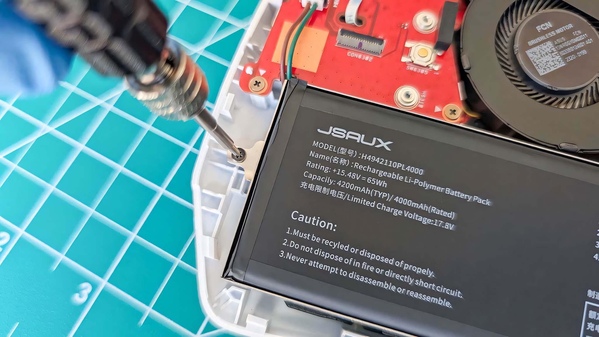 A gloved hand using a screwdriver to secure a screw on the new JSAUX battery in the open ROG Ally.