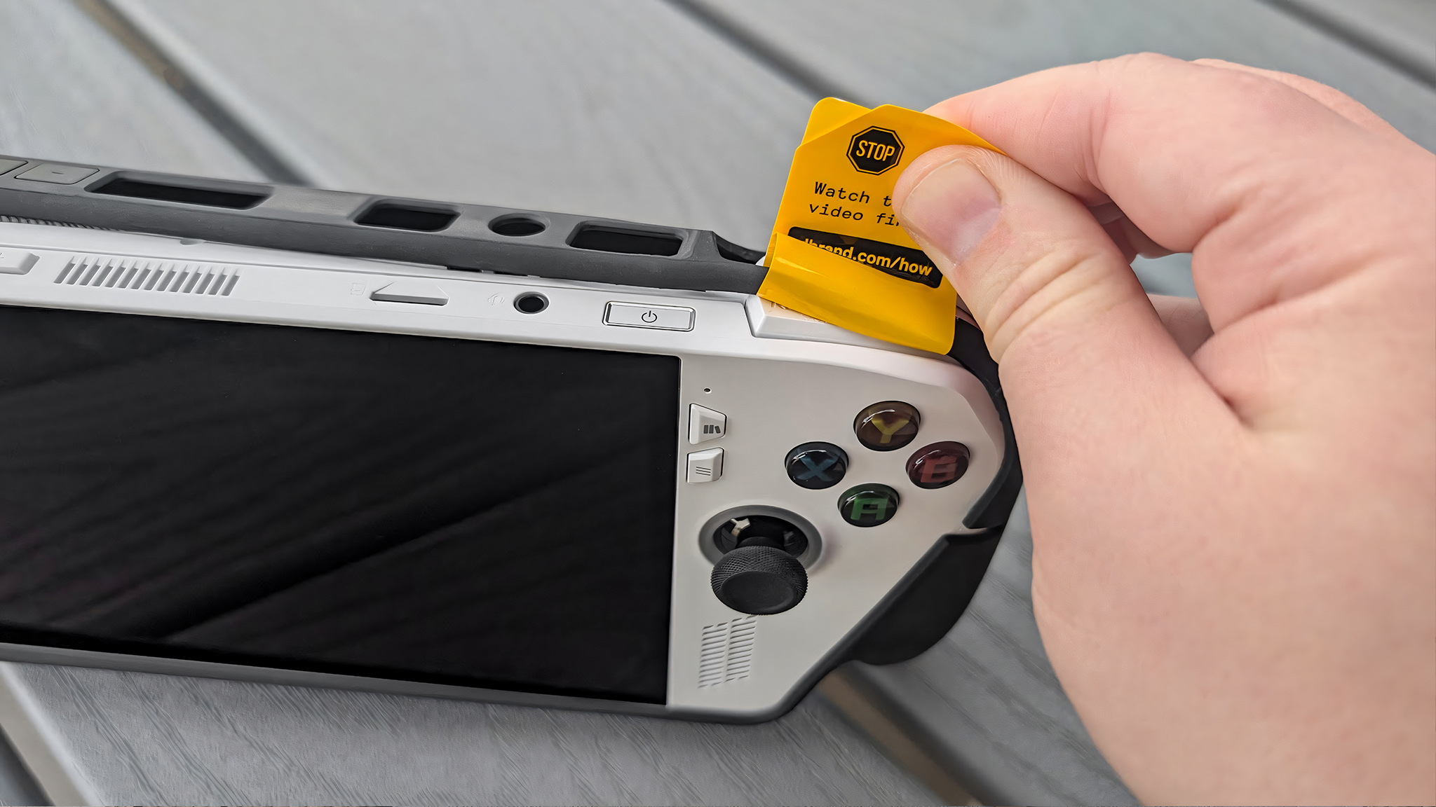 Рука тянет за желтую установочную наклейку, обернутую вокруг верхней части dBrand Killswitch.