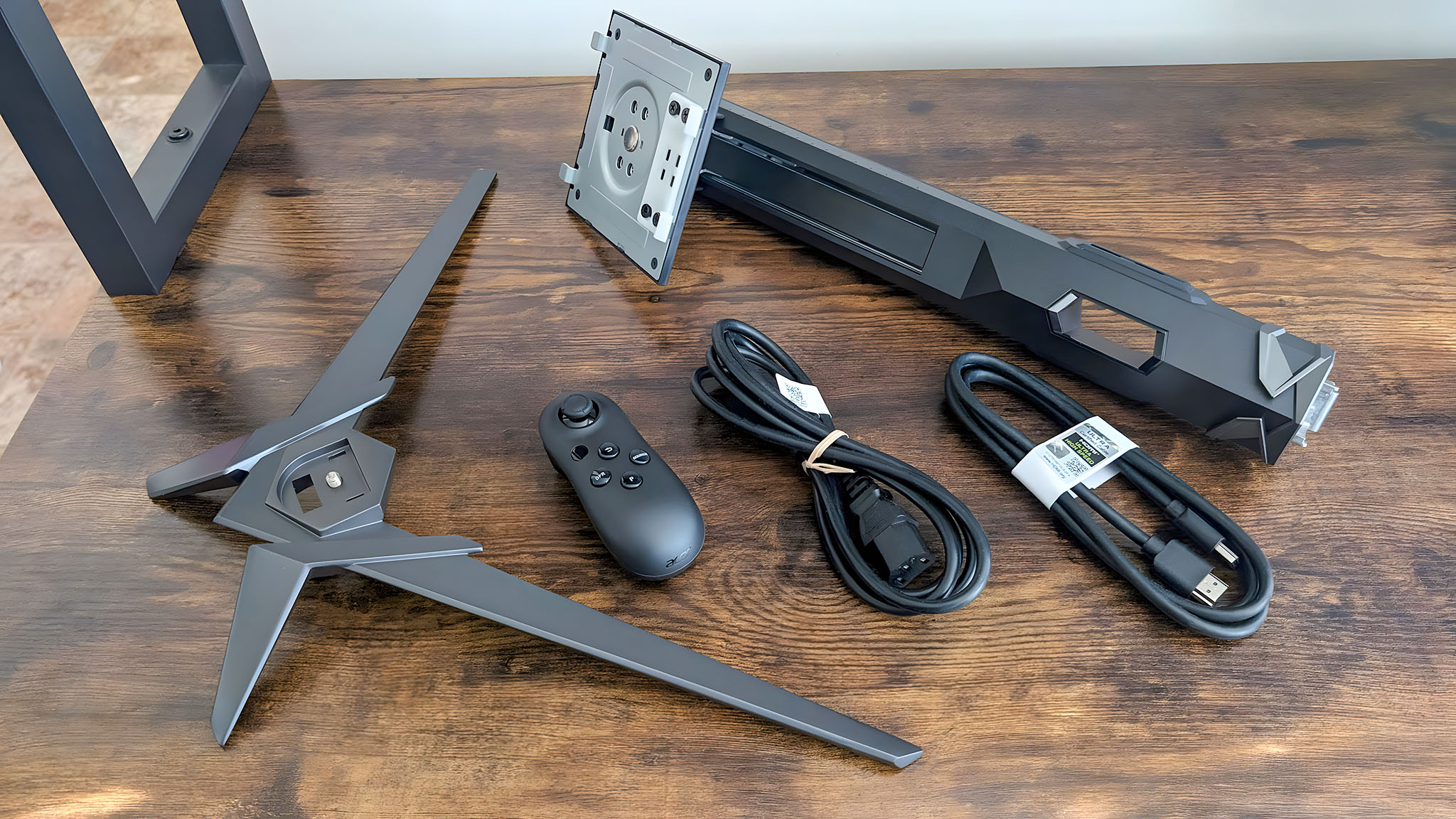 The Acer Predator XB273K's stand, base, remote, HDMI cable, and power cable on a desk.