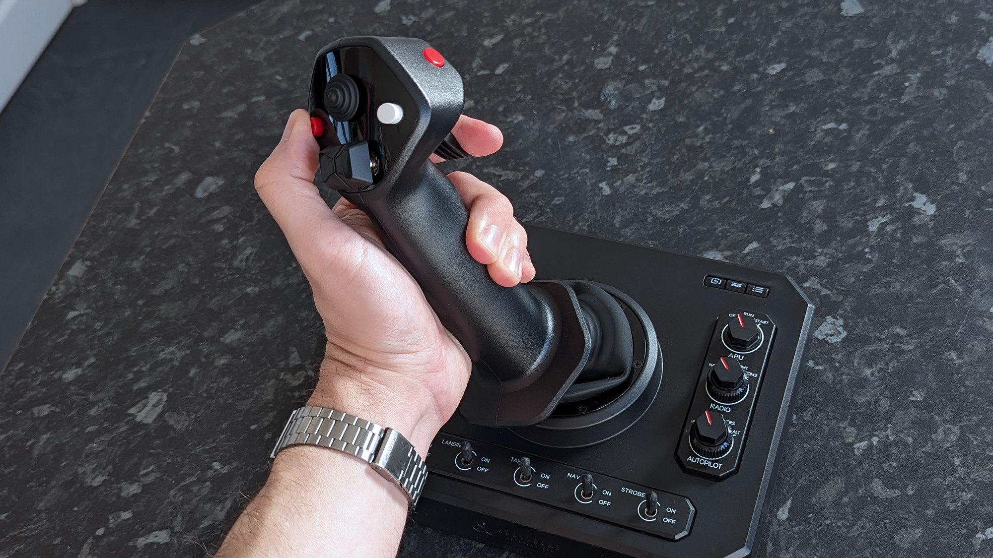 Рука держит джойстик Honeycomb Aeronautical Foxtrot Aviation Stick на столе с мраморным узором