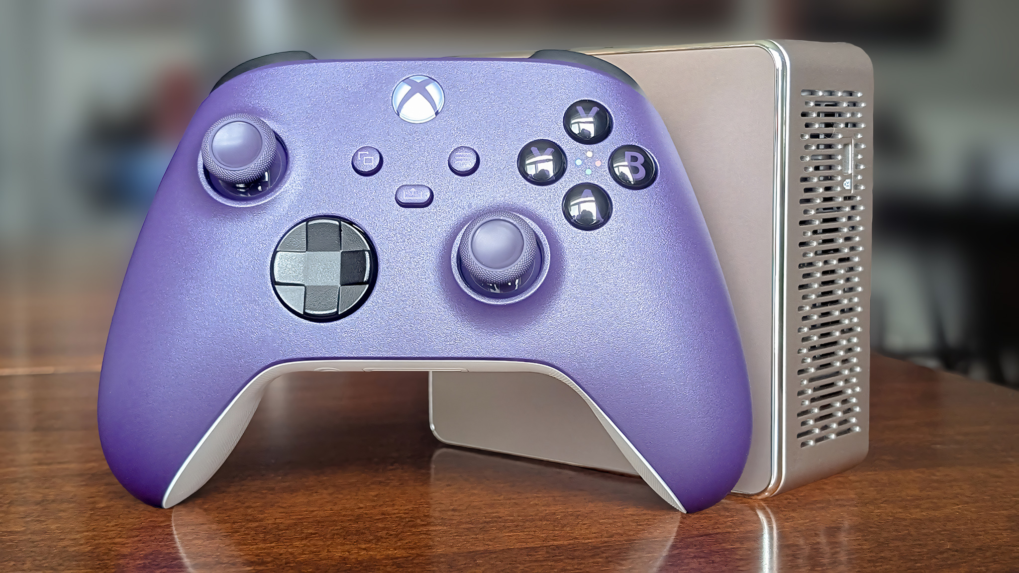 A purple Xbox Controller with a Geekom mini PC standing upright on a table.