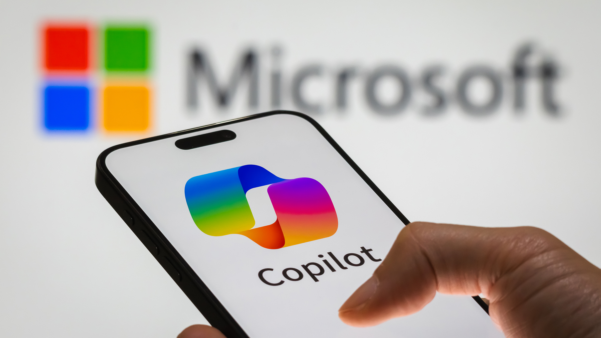 Телефон с отображением Copilot перед экраном с надписью Microsoft.
