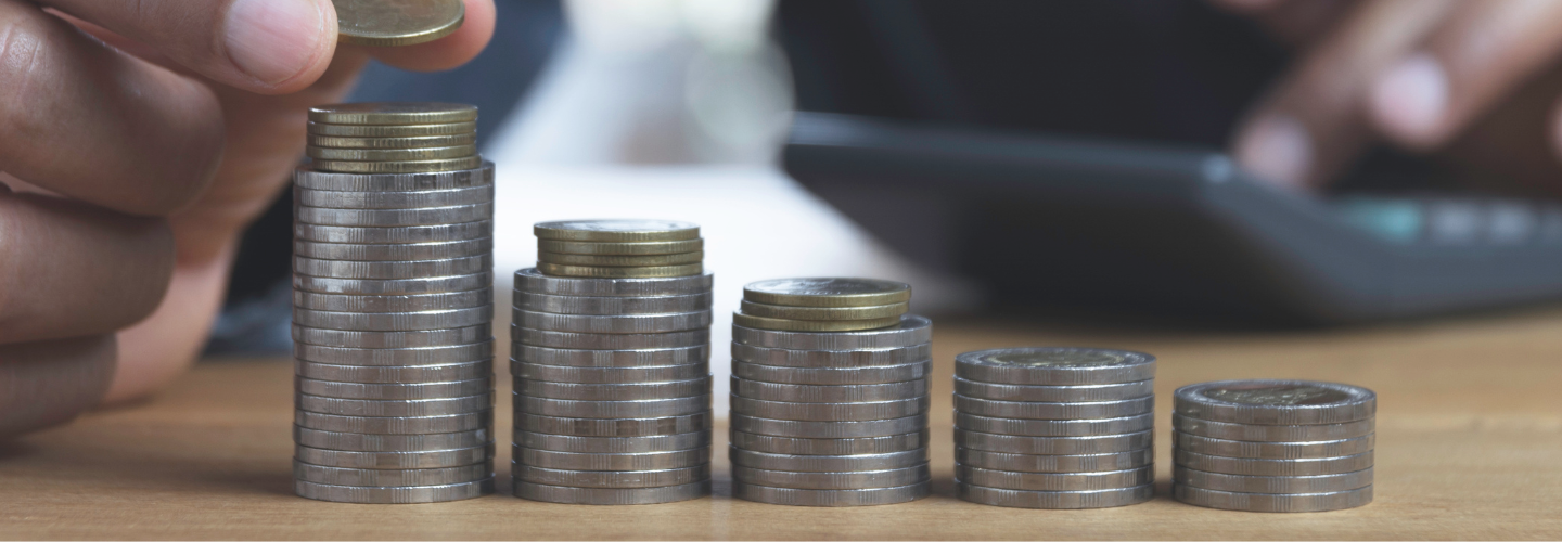 Close up of a hand placing a coin on a stack of coins. 