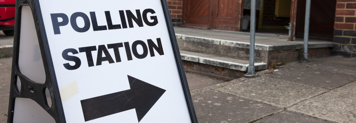 A sign with text reading Polling Station with an arrow pointing right outside a building.