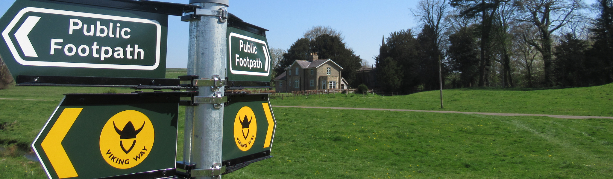 An image of a public footpath sign and background of a field and house.