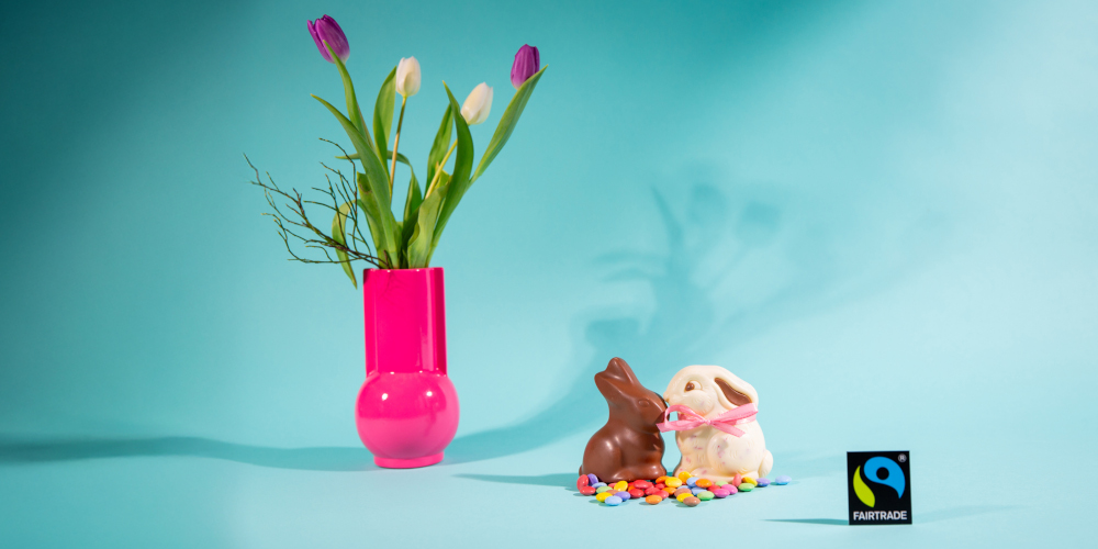 Faire Schokoosterhasen in braun und weiß zwischen dem Fairtrade-Siegel und einer Vase mit Tulpen