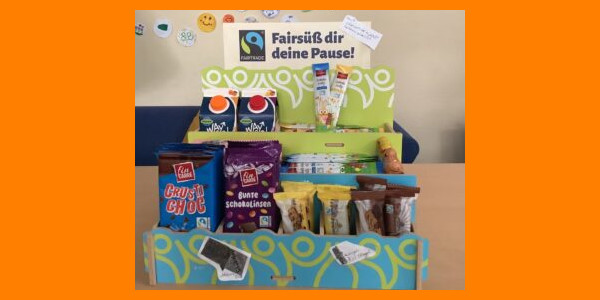 Verkaufsaufsteller mit fairen Süßigkeiten und dem Titel "Fairsüß dir deine Pause", daneben das Fairtrade-Siegel