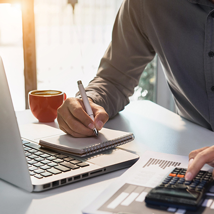 Mann am Schreibtisch mit Laptop und Taschenrechner. 
