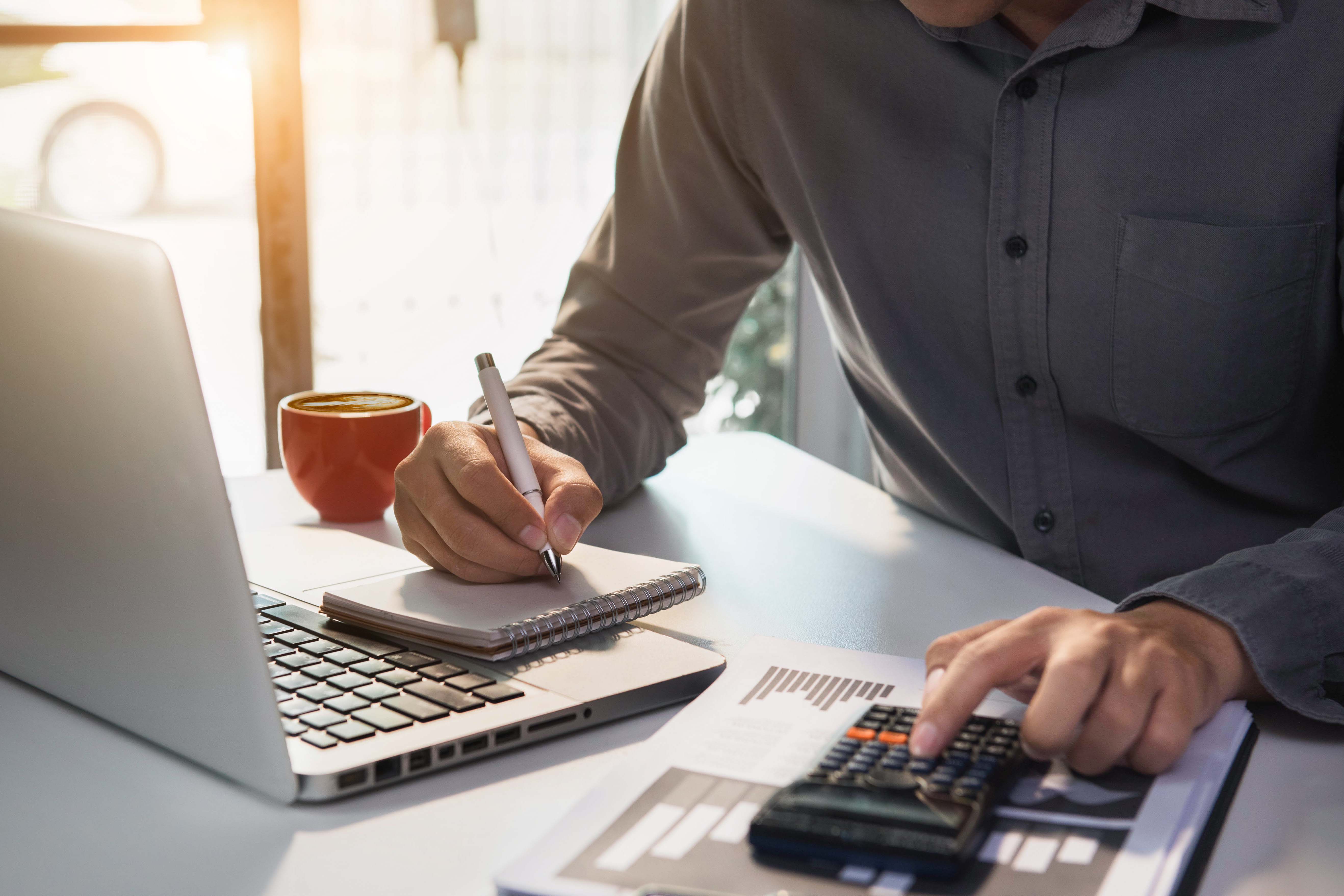 Mann vor Laptop, mit Zettel und Stift und Taschenrechner