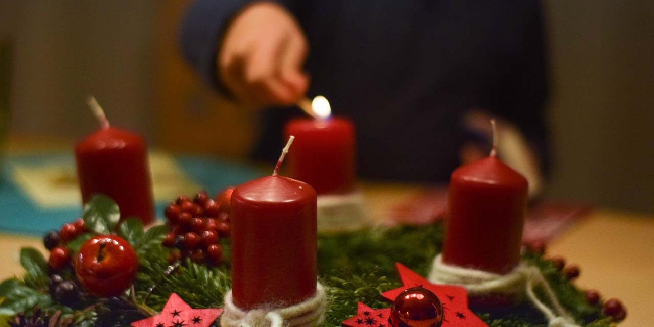Hand zündet Kerze auf Adventskranz an
