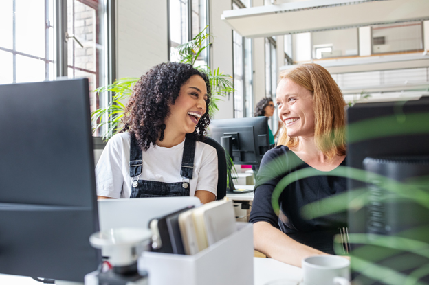 Frauen am Schreibtisch lachen sich an