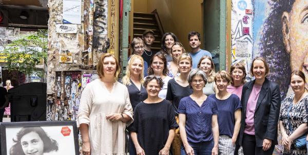 Gruppenfoto von Mitarbeitenden des Anne Frank Zentrums vor einem Eingang mit Wandbild.