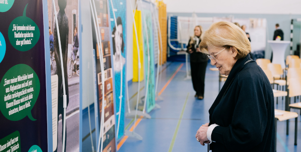 Eine ältere Frau steht vor mehreren Ausstellungstafeln mit Fotos und Infotexten.