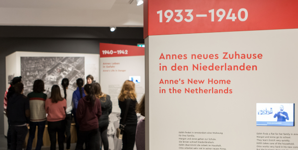 Jugendliche stehen in einer Ausstellung; daneben zwei Ausstellungswände mit Textelementen sowie Videos in DGS