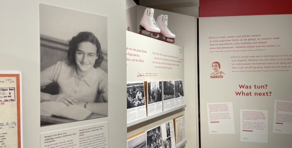 Ausstellungssegment mit einem historischen Porträtfoto von Margot Frank, Text- und Bildtafeln sowie einem Paar weißer Schlittschuhe als Ausstellungsobjekt.