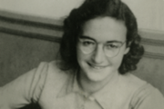 Porträt von Margot Frank, einer jungen Frau mit schulterlangem, lockigem Haar und Brille, das lächelt.