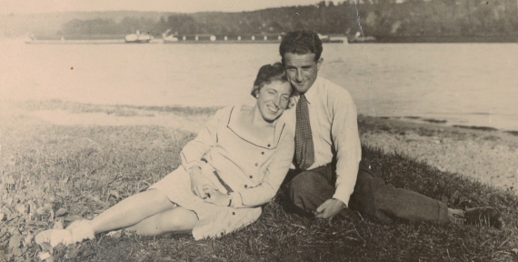 Eine Frau und ein Mann liegen sich lächelnd auf einer Wiese in den Armen.