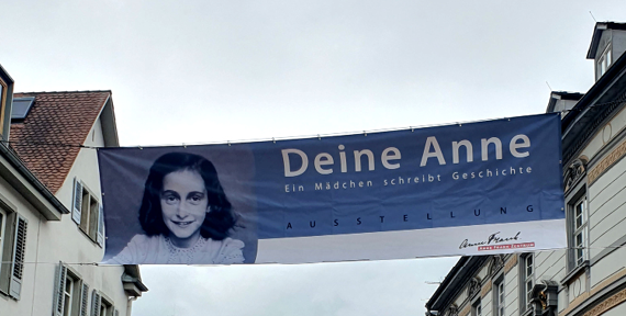 Ein großer Banner mit Schriftzug und Portrait von Anne Frank hängt zwischen zwei Häusern.