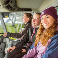 Drei junge Erwachsene sitzen in einer Landmaschine und blicken in die Kamera