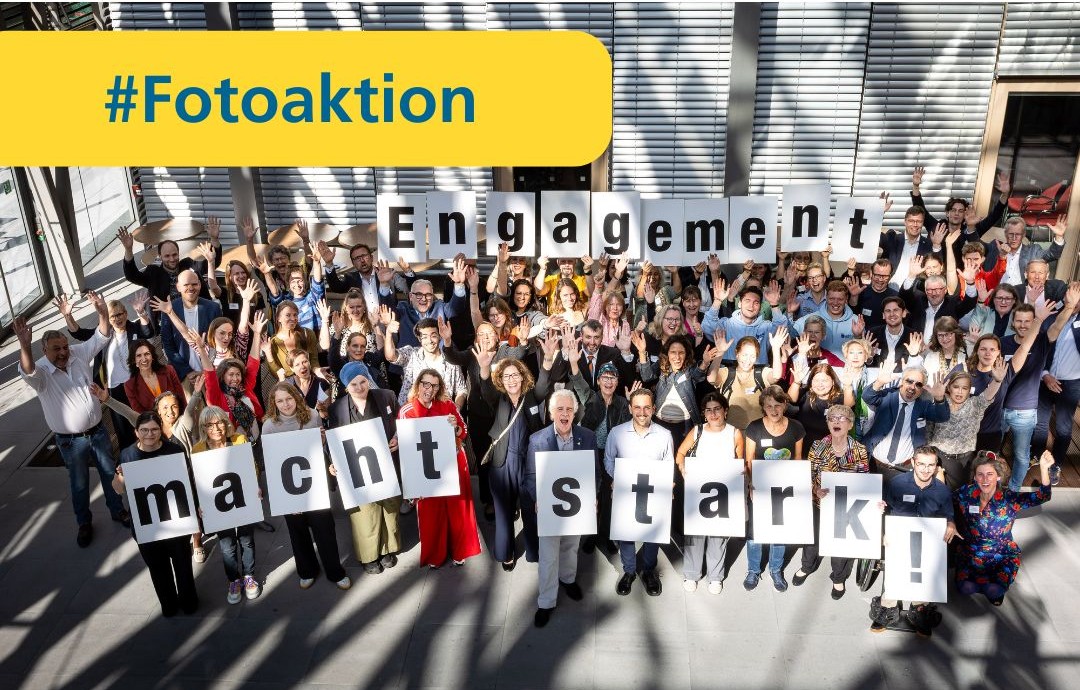 Eine Gruppe von Menschen steht nebeneinander vor einer Wasserkante am Hafen und halten Buchstaben hoch.