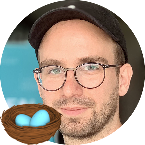 Junger Mann mit schwarzer Kappe, Bart, runder Brille, davor Nest-Emoji