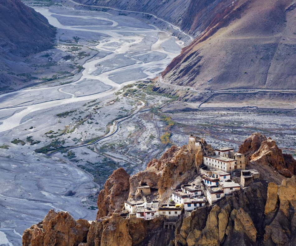 Das Bild zeigt ein Tal im Himalaja. Im Vordergrund sieht man auf einer steilen Anhöhe ein kleines Dorf, im HIntergrund schlängelt sich ein Fluss durchs Tal.