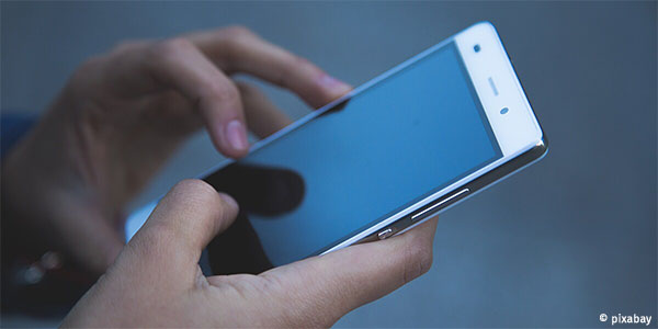 Hände hatlen ein Handy in der Hand. Der Bildschirm ist schwarz. Die linke Hand ist bereit den Bildschirm zu berühren.