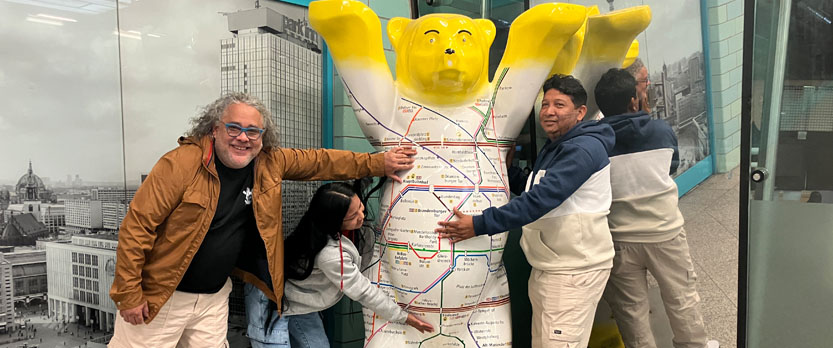 Drei Personen um den Berliner Bär herum, der das Berliner U-Bahnnetz auf sich abgebildet hat