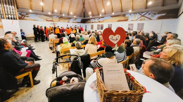 Auf dem Bild sieht man eine Menschenmenge in der Kirche Grafrath. Vorn steht ein Chor. Im Vordergrund des Bildes sieht man einen Spendenkorb, darin ein Herz aus rotem Papier, auf dem steht: Danke!