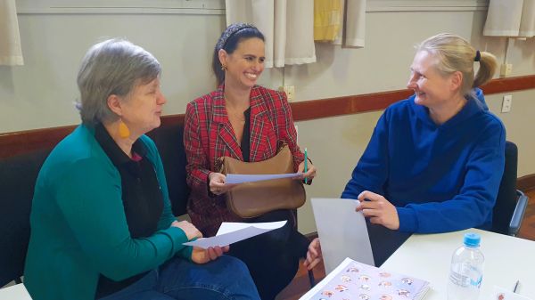 Auf dem Bild sieht man drei Frauen mit Bildern in der Hand, die sich ansehen und über etwas lachen.