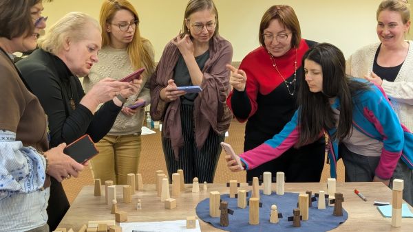 Sieben Frauen stehen um einen Tisch herum. Auf dem Tisch sind Bausteine aufgebaut. Die Frauen diskutieren und machen Fotos.