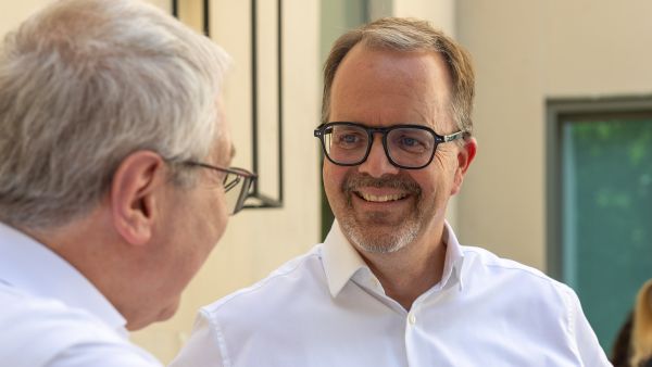 Markus Rinderspacher wendet sich lächelnd einem Gesprächspartner zu, der im Vordergrund nur von hinten zu sehen ist.