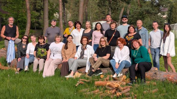 Auf dem Bild sieht man die Seminargruppe. In der ersten Reihe sitzen neun Frauen auf einem Baumstamm. Dahinter stehen 12 Männer und Frauen sowie der Trainer.