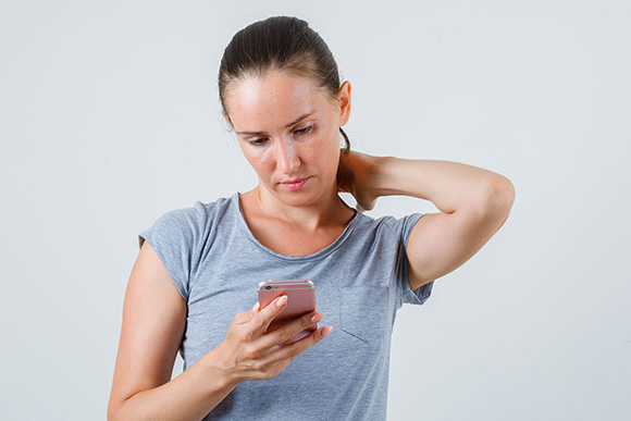 Frau greift sich in den Nacken und hält ein Handy in der Hand | Foto: freepik