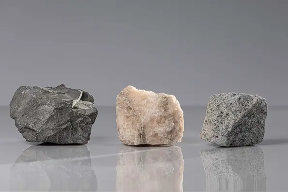 Auf einer spiegelglatten Fläche liegen drei Steine nebeneinander. Es handelt sich um die für die Endlagersuche für hochradioaktive Abfälle in Frage kommenden Wirtsgesteinstypen Ton, Salz und Kristallin.