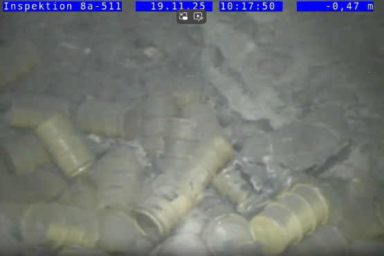 Foto von übereinanderliegenden gelben Fässern in einem Bergwerk. Die Fässer sind teilweise mit Staub bedeckt und verformt.