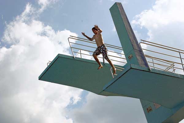 Aufnahme aus der Froschperspektive: Ein Kind in Badeshorts springt von einem Sprungturm in einem Freibad.