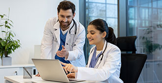 Junge Ärztin und junger Arzt schauen sich gemeinsam etwas auf einem Laptop an