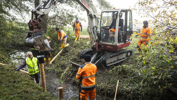 Arbeiten an einem Bach mit Bagger und Gruppe von Arbeitern