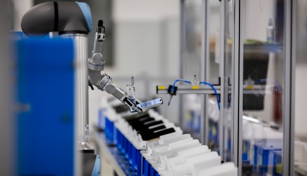 Ein Roboter greift bei Rebuy ein Smartphone um es in ein Gradinggerät zu plazieren. 