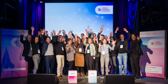 Die 12 Projektteams des Civic Coding-Accelerator-Programms 2024 stehen auf der Bühne vor einem bunten Banner mit der Aufschrift „Digital Gipfel 2024“.