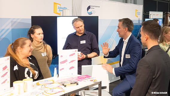 Foto von Niclas Schmidt, das eine Gruppe Menschen auf der Jahrestagung der Zukunftszentren im Gespräch zeigt.