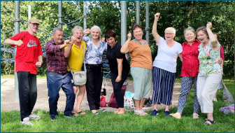 Gruppe von älteren, begeisterten Menschen auf einer Wiese vor Bäumen.