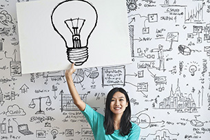 Sketchnotes - einfach zeichnend denken Eine junge Frau sitzt vor einer Wand mit vielen kleinen Skizzen und hält eine große Skizze einer Glühbirne in der Hand