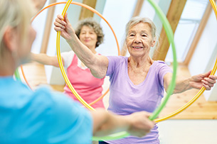2. Aktionstag Ältere und Hochaltrige Zu sehen sind hochaltrige, fitte und fröhliche Frauen bei einer Gymnastikübung mit dem Reifen in einer Sporthalle.