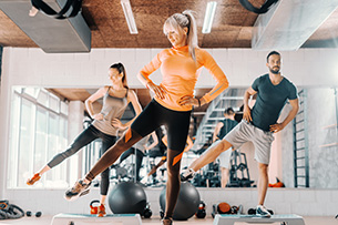 Aktionstag Fitness 2026 Drei junge Menschen sind in einem FitnessStudio s und führen ein Step Aerobic Workout aus.
