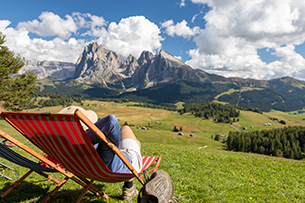 Bildungsurlaub Aktiv gegen Stress - Erkennung, Entwicklung und Nutzung von Ressourcen und Handlungsmöglichkeiten im beruflichen Kontext Eine Wanderin sitzt auf einer Anhöhe auf der Seiser Alm im Liegestuhl mit Blick auf die Berge