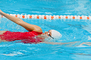 Zu sehen ist eine Frau im Wasser in einem Schwimmbad. Sie schwimmt die Schwimmtechnik Rückenschwimmen