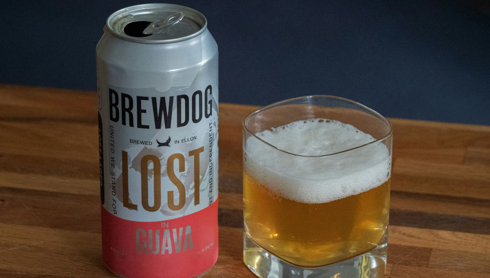 An open can of BrewDog’s “Lost in Guava” on a wooden table, next to a tumbler containing beer (Photo: Brett Jordan on Unsplash)