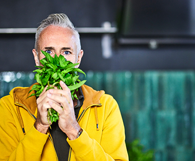 Grauhaariger Mann riecht an einem Bund Basilikum
